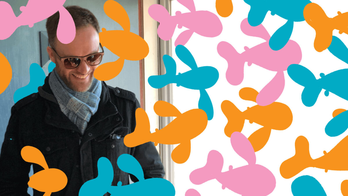 Mal Jones, dressed in a jacket and scarf smiling and laughing. Illustrated fish are swimming around him.